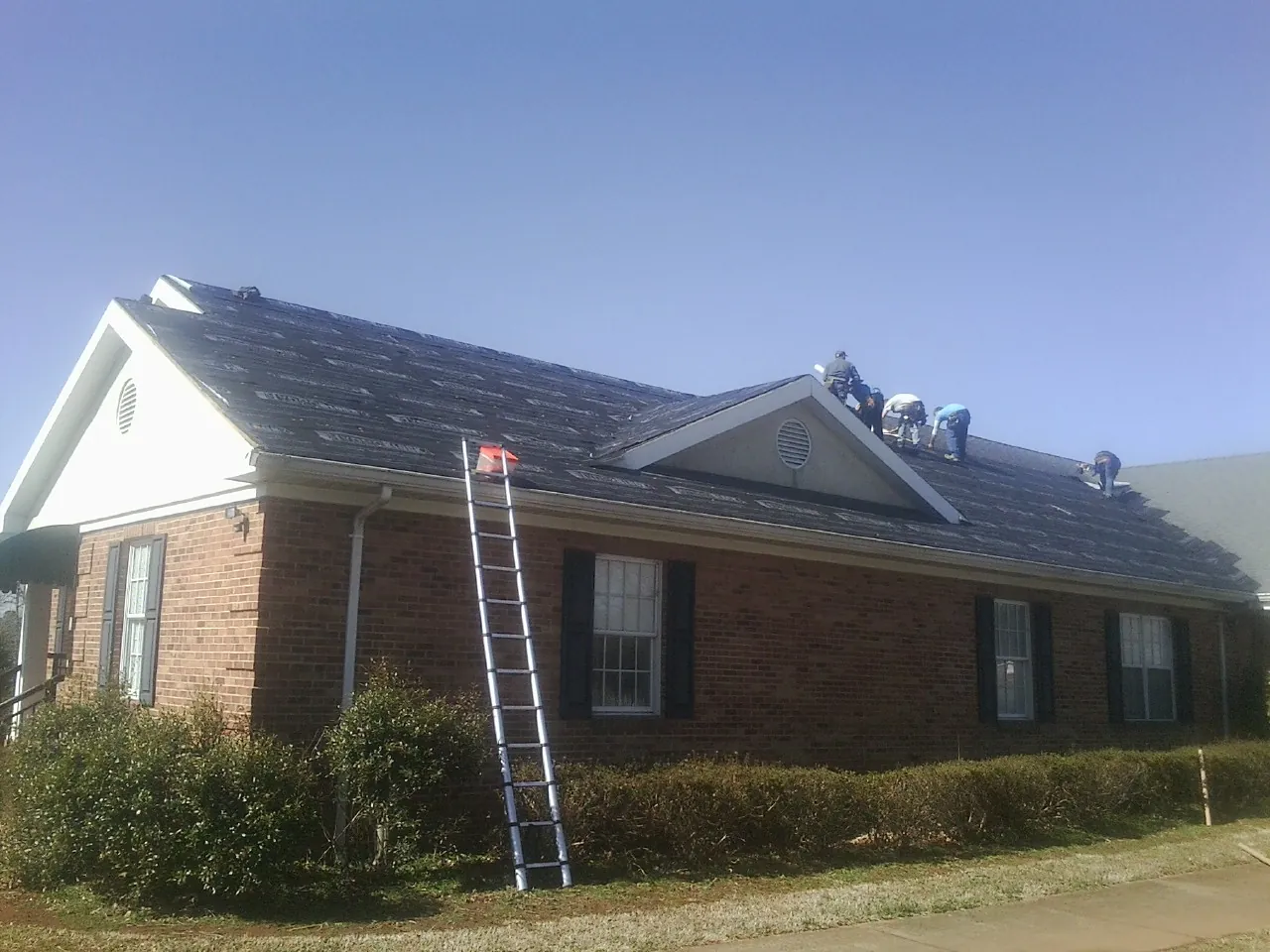 Crew tearing shingles off a brick ranch roof with a ladder set — Emergency Roof Repair work by our crew in Mishawaka