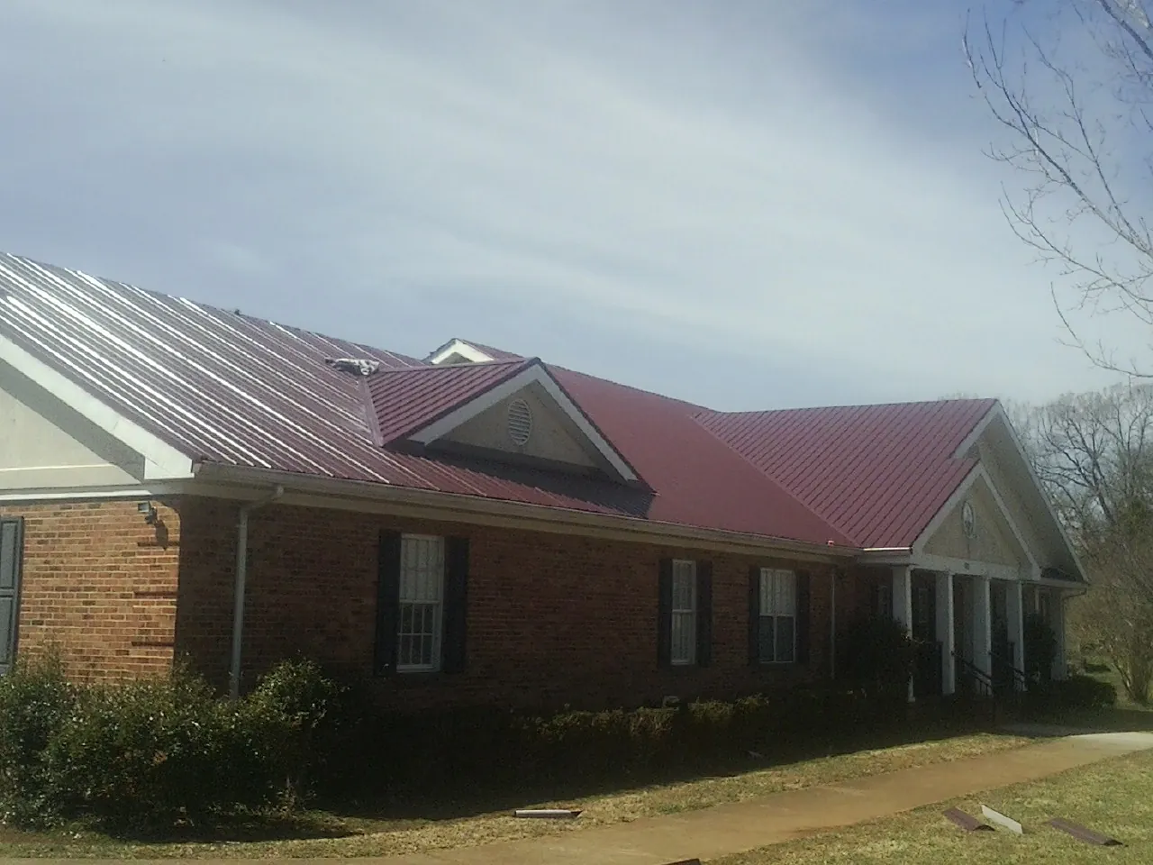 Red metal roof with gabled entries on a long brick building, from a Hail Damage Roof Repair job in Mishawaka