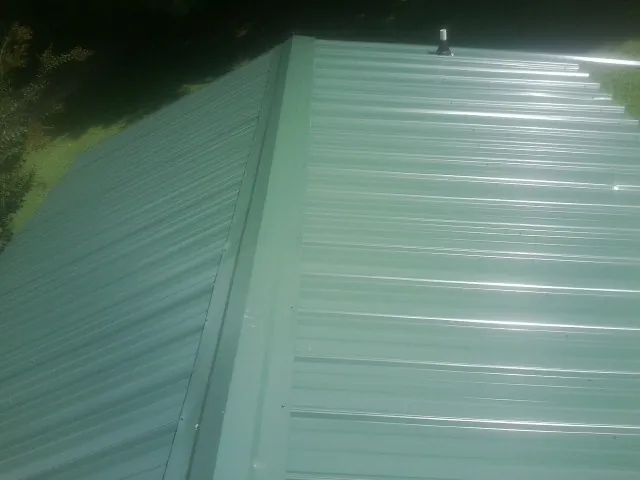 New green metal panels meeting at the ridge of a roof — Flat Roof Repair work by our crew in Mishawaka