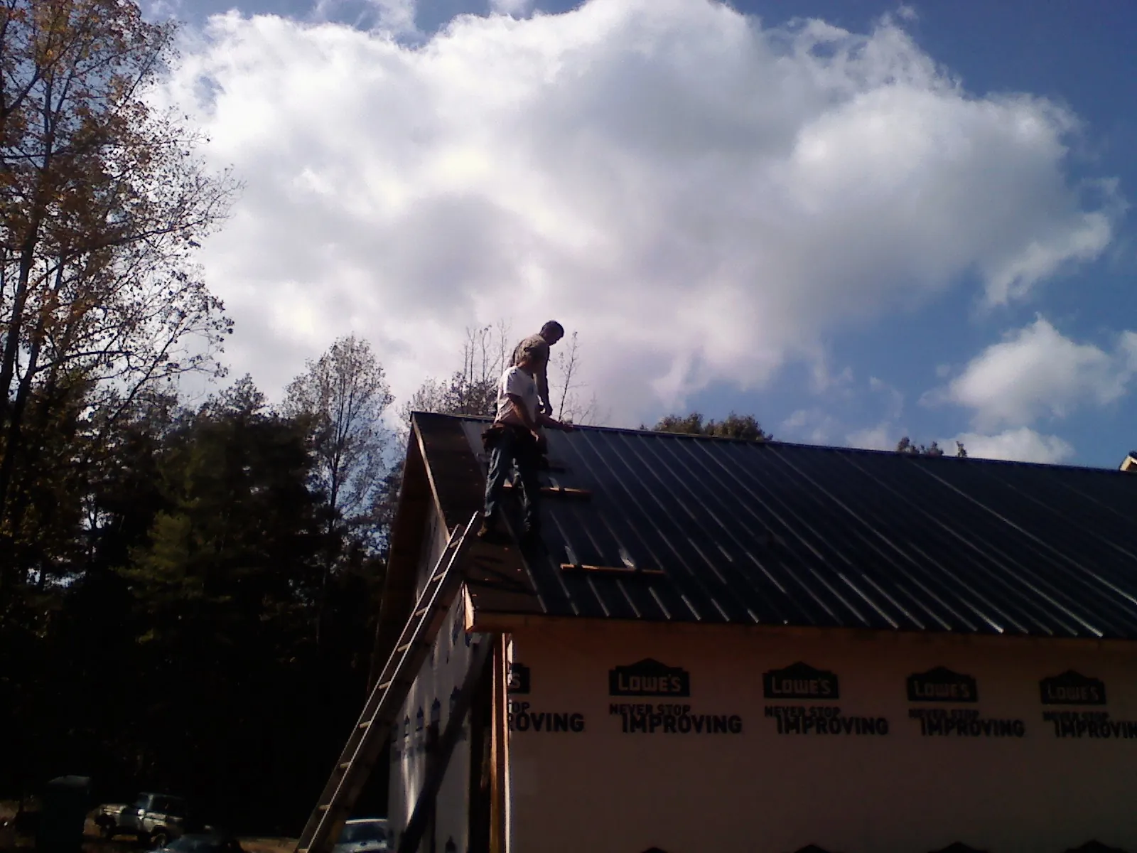 Roofer fastening dark metal panels high against a cloudy sky, from a Roof Inspection job in Mishawaka