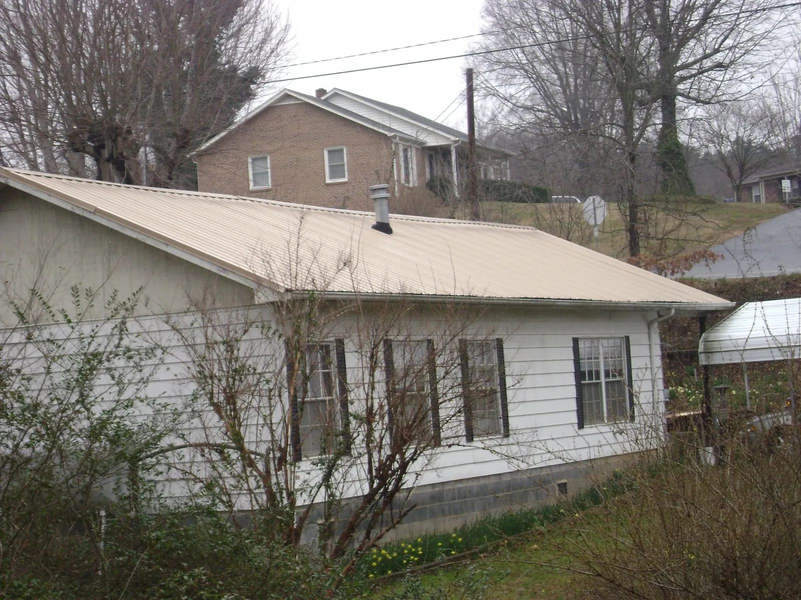 Tan metal roof on a white sided house set into a hillside — Commercial Roofing by Roofing Brothers in Mishawaka
