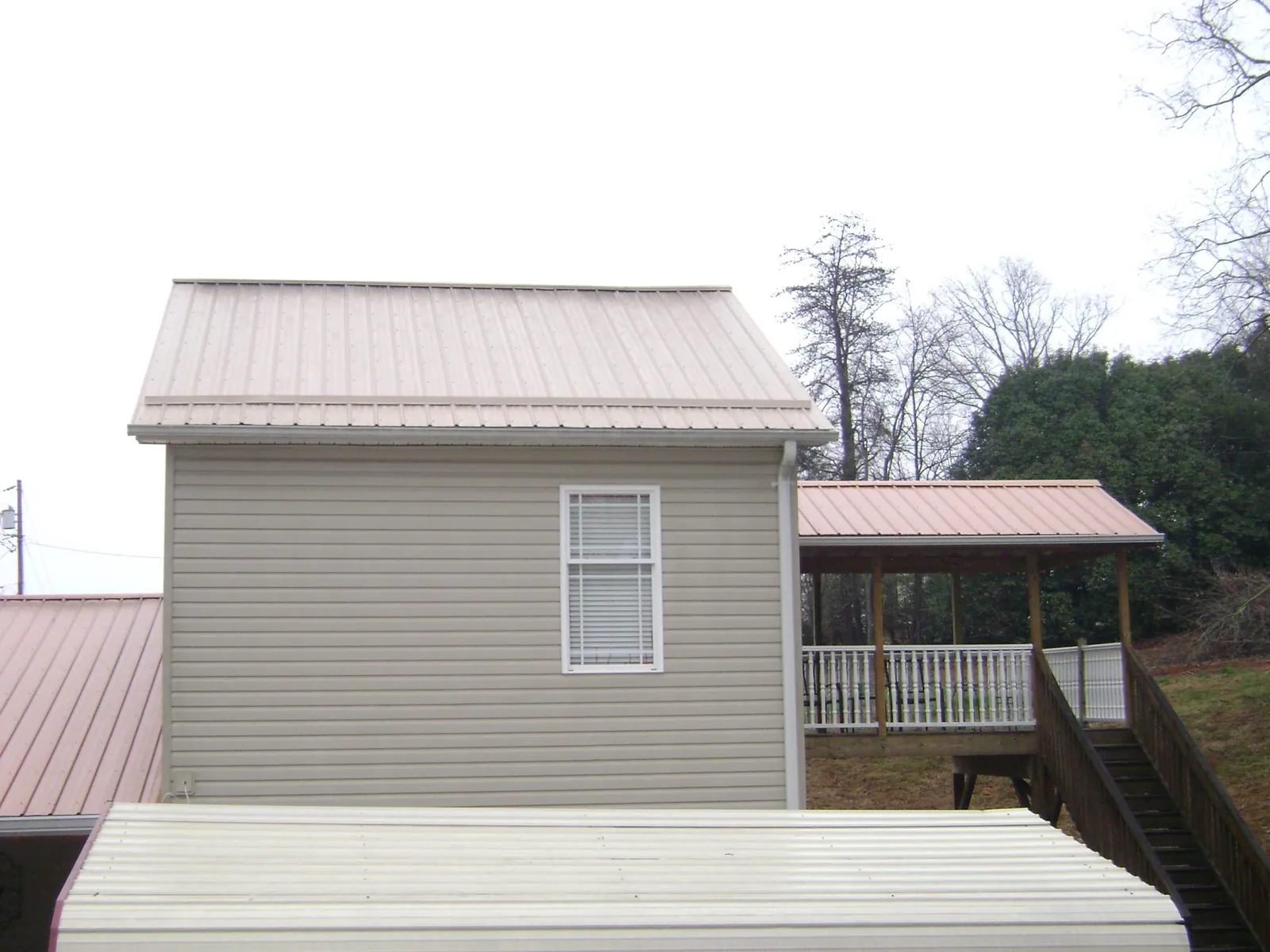 Tan metal roofs on a two story addition and attached porch, from a Roof Replacement job in Mishawaka
