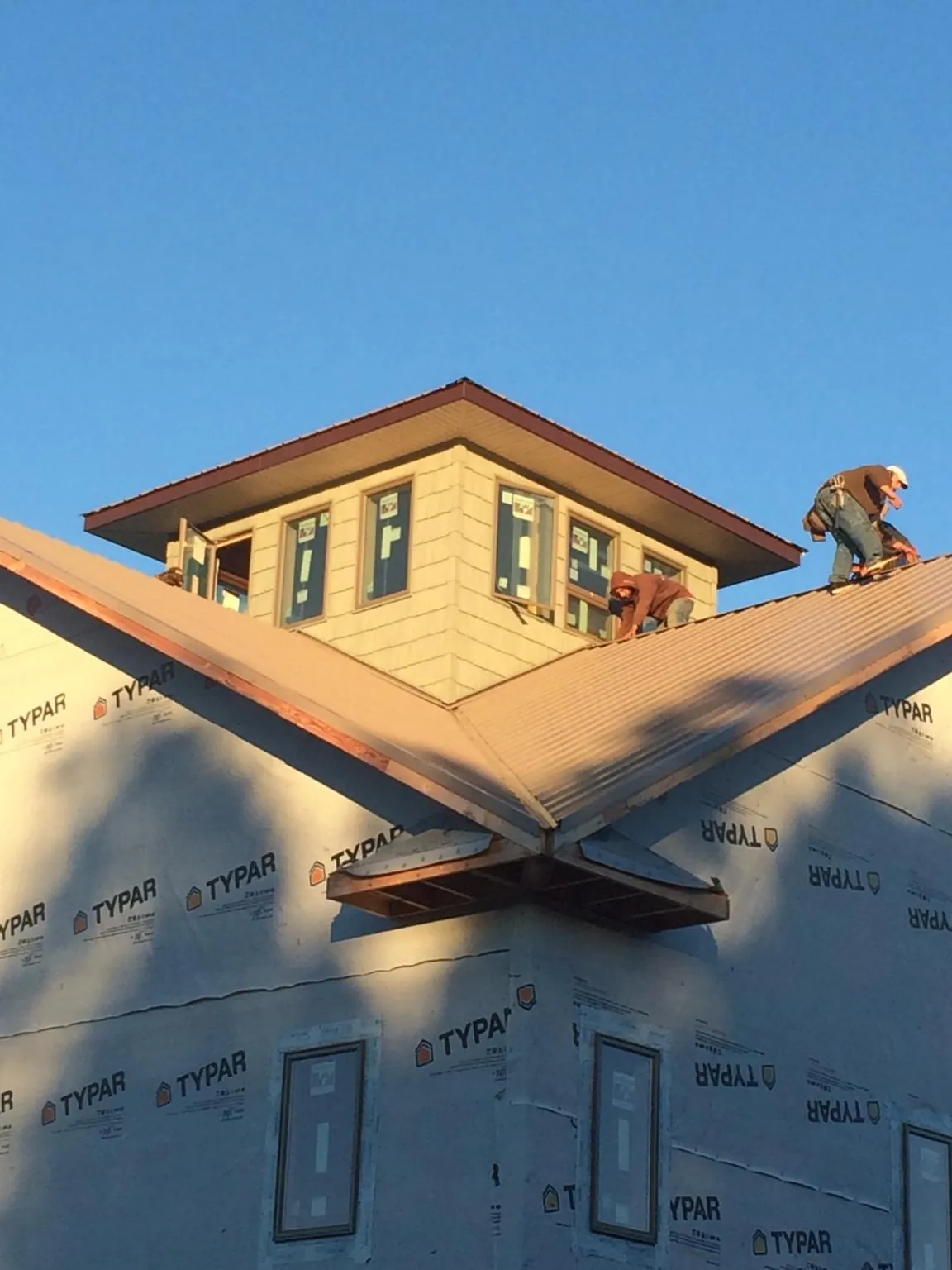Roofers working around a rooftop cupola on a new metal roof at sunset — Roof Waterproofing in Mishawaka by Roofing Brothers